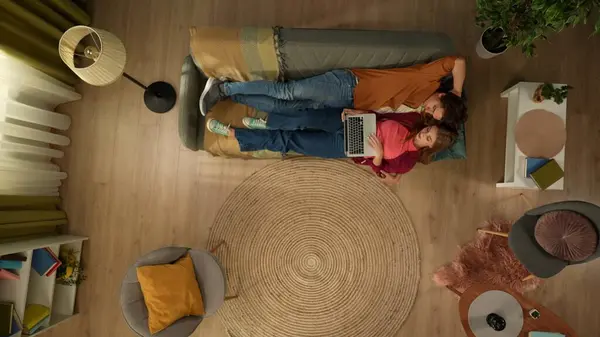 在头像中 一对年轻夫妇躺在沙发上 依偎在一起 聊着天 看着笔记本电脑屏幕 好像在网上寻找什么似的 网上购物 — 图库照片