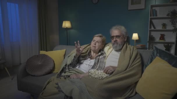 フレームには 高齢のカップルがソファーの下に座っています 彼らはテレビで映画や番組を見たり ポップコーンを食べたりしている Hdr Bt2020 Hlg材料について — ストック動画