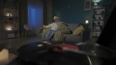 Kapalı çekim, dönen diski olan vinil bir plak çalar gösteriyor. Arka planda, yaşlı bir çift bir kanepede oturuyor. Adam kameraya bakar ve müzik dinler. HDR BT2020 HLG