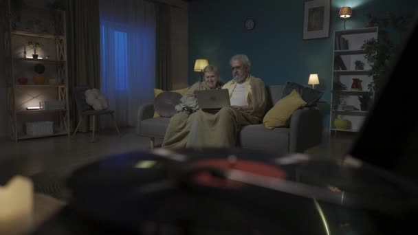 クローズアップ画像は 回転ディスクを持つビニールレコードプレーヤーを示しています 高齢のカップルは ラップトップとソファーに座って ビデオ通信を通じて誰かと話しています Hdr Bt2020 Hlg材料について — ストック動画