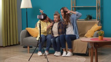 Kıdemli aile üyesi yaşam konsepti. Aile portresi. Yaşlı kadının, kızının ve küçük oğlunun oturma odasındaki kanepede oturup tripodla akıllı telefondan selfie çekerken yakın plan..