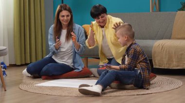 Kıdemli aile üyesi yaşam konsepti. Aile portresi. Son sınıf öğrencisinin resmi, günlük kıyafetler içinde, kızı ve çocuğu boyayla oynarken, beyaz kağıda el izi bırakırken..