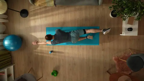 Top view capturing a young man doing his morning yoga exercise, stretching, pulling arms and legs. Home, room, indoor activities. Healthy and active lifestyle, morning routine, achieving the goals.