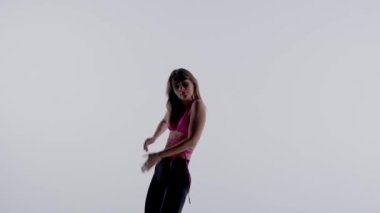 Parlak pembe sutyen giyen genç bir kadın, üst, taytlar ve yüksek topuklu ayakkabılar stüdyoda dans ederken izole edilmiş beyaz bir arka plan. Orta boy. Reklam, yaratıcı içerik.