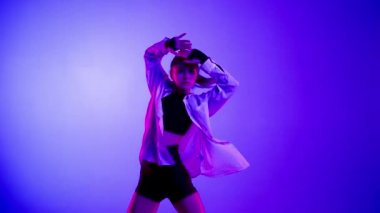 Stüdyoda üstsüz, şortlu ve tişörtlü genç bir kadın duygusal dans gösterisi yapıyor. Neon mavi, pembe ve kırmızı renk şeması, ombre, gradyan arkaplan. Orta boy..