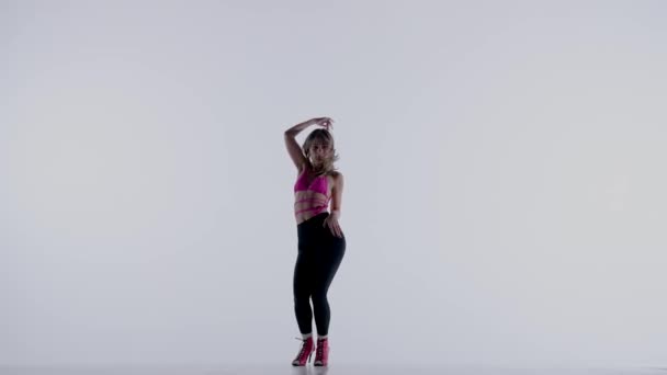 身穿明亮的粉色胸罩 腿和高跟鞋的年轻女子在演播室里跳着精力充沛的高跟鞋 与外界隔绝的白色背景 全身而退广告 创意内容 — 图库视频影像