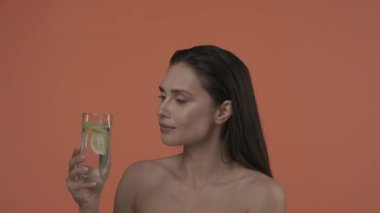 Güzel esmer modelin portresi. Doğal makyajlı ve gülümseyen bir kadını yakından çek. Cilt bakımı reklam konsepti. Çekici kadın bardağı su ve limon dilimleriyle tutuyor, içiyor.