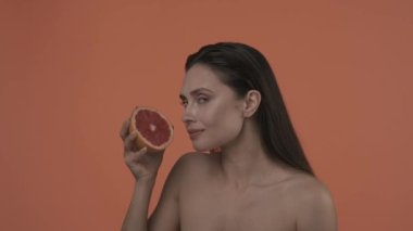 Güzel esmer modelin portresi. Doğal makyajlı ve gülümseyen bir kadını yakından çek. Cilt bakımı reklam konsepti. Çekici bir kadın, elinde dilimlenmiş greyfurtla onu sıkıyor ve gülümsüyor.