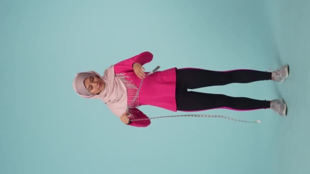 全尺寸的孤立视频拍摄了一个穿着运动服和头巾的迷人的年轻女子 她笑着测量她的腰围 减肥场所 — 图库视频影像