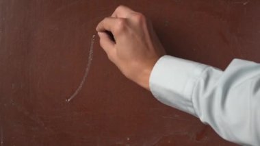 Kalıplı kahverengi karatahta arka planı. Erkek el, Pi değeri yazıyor. Tahtada 3.14 numara. Yakından bir parça beyaz tebeşirle. Eğitici ve yaratıcı içerik, okul kavramı.