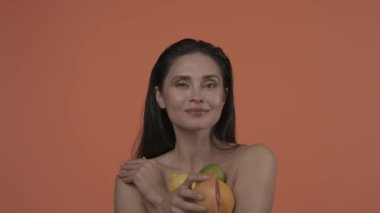 Güzel esmer modelin portresi. Doğal makyajlı ve gülümseyen bir kadını yakından çek. Cilt bakımı. Elinde dilimlenmiş greyfurt ve gülümseyen diğer sitrusları tutan çekici bir kadın. Ağır çekim. HDR