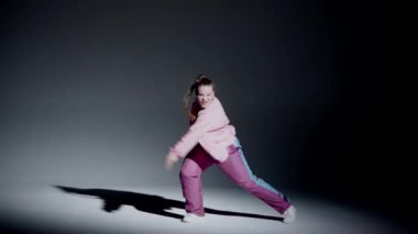 Stüdyoda dans eden çekici bir kadın. Siyahtan beyaza yumuşak eğimli arka plan, beyaz spot ışığı ve belirgin düşen gölge. Modern koreografi. Tam boy. Promosyon klibi ya da