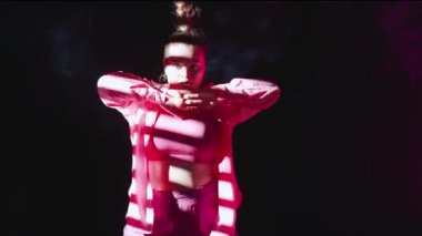 Stüdyoda dans eden çekici bir kadın. Siyah arka plan dumanla, beyaz spot ışığı ve düşen çizgili gölgeyle dolu. Modern koreografi. Orta boy. Reklam videosu veya reklamı.