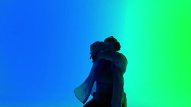 Stüdyoda yeşil ve mavi neon arka planda dans eden bir kadının silueti. Modern dinamik ve enerjik dans koreografisi. Orta boy. Yaratıcı içerik, tanıtım videosu veya reklam