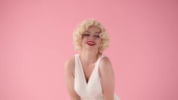 穿着假发 白色衣服 嘴唇上涂着红色唇膏 背景是粉色的年轻快乐女人的画像 女主角玛丽莲 梦露模仿自己的动作 摆出一副姿势 — 图库视频影像