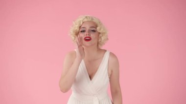 Elini ağzına koyan kadın çığlık atıyor, birini arıyor. Stüdyoda Marilyn Monroe 'nun pembe arka planında bir kadın.