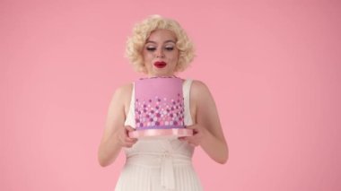 Çekici kadın heyecanlı bir şekilde doğum günü pastasını gösteriyor. Doğum gününü kutlayan kadın, zafer, başarı. Marilyn Monroe 'nun stüdyodaki pembe arka plandaki görüntüsü.