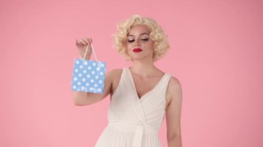 Elinde iki küçük hediye çantası tutan bir kadın, mavi ve pembe. Pembe arka plandaki Marilyn Monroe 'ya benzeyen bir kadın. Alışveriş, satış, tatil konsepti