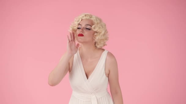 叫び声を上げ 誰かを呼び出し 発表する彼女の手を持つ女性 ピンクの背景にあるスタジオでマリリン モンローをイメージした女性 — ストック動画
