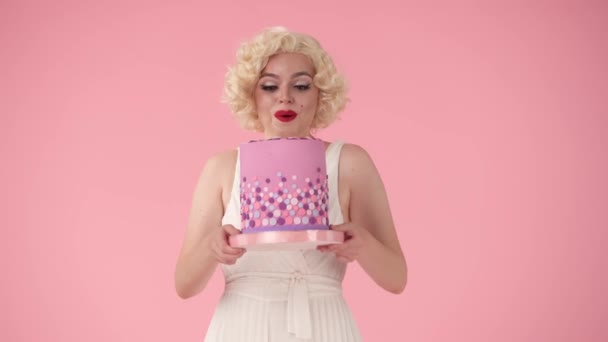 迷人的女人兴奋地炫耀着生日蛋糕 女人庆祝生日 照片中的女人玛丽莲 梦露在一个粉色背景的工作室里 — 图库视频影像