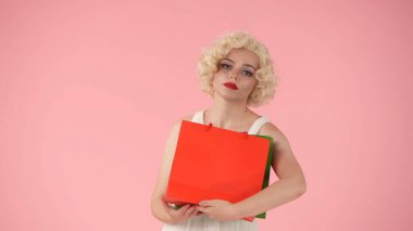 Alışveriş yorucu olabilir. Elinde alışveriş poşetleri olan yorgun görünüşlü bir kadının portresi. Marilyn Monroe 'nun stüdyodaki pembe arka plandaki görüntüsü. Alışveriş konsepti