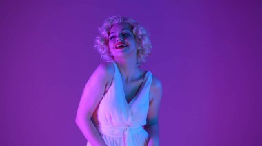 Marilyn Monroe 'nun görüntüsündeki çekici bir kadının portresi. Beyaz elbiseli, parlak makyajlı, stüdyoda peruklu, pembe ve yeşil ışıklı bir kadın.