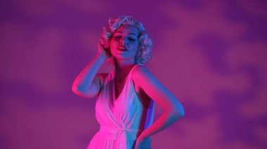 Marilyn Monroe 'nun görüntüsündeki çekici bir kadının portresi. Beyaz elbiseli, parlak makyajlı, stüdyoda peruklu pembe ve yeşil ışıklı bir kadın.