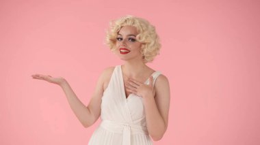 Kadın elini yana doğru tutar, tavsiye eder. Marilyn Monroe 'nun stüdyodaki pembe arka plandaki görüntüsü. Reklam, tanıtım, kopyalama alanı