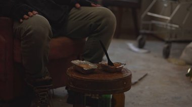 Terk edilmiş bir binanın odasında oturan tanınmayan evsiz zavallı adam. Çöpten yapılmış, tek kullanımlık sofra takımında yiyecek olan bir masa. Evsizlik ve yoksulluk, işsizlik, kriz.