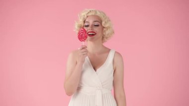Neşeli bir kadın, şaşırmış, renkli bir lolipop gösteriyormuş. Bir kadın tatlı şekeri çubukta yalıyor, gözünü lolipopla kaplıyor ve öpüyor. Marilyn Monroe 'nun suretindeki kadın