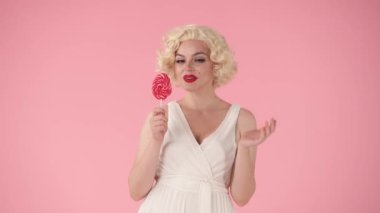 Neşeli bir kadın, şaşırmış, renkli bir lolipop gösteriyormuş. Kadın mutlu bir şekilde çubuktaki şekeri yalıyor, dişleriyle lolipopu ısırıyor. Marilyn Monroe 'nun stüdyodaki görüntüsü...