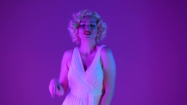 Stüdyoda Marilyn Monroe 'nun pembe ve yeşil neon ışıklı görüntüsü. Kadın selamlama işareti olarak el sallıyor ve hava öpücüğü gönderiyor.