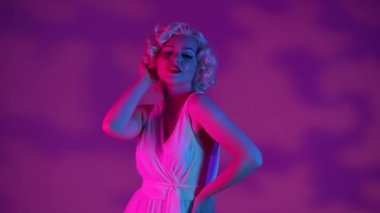 Pembe arka planda pembe ve yeşil neon ışıklı stüdyodaki Marilyn Monroe 'ya bakan bir kadın. Kadın havadan bir öpücük yolluyor.