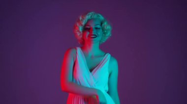 Kadın dans ediyor, eğleniyor, hava öpücüğü gönderiyor. Marilyn Monroe 'nun görünüşünde bir kadın stüdyoda çok renkli neon ışıkta dans ediyor.