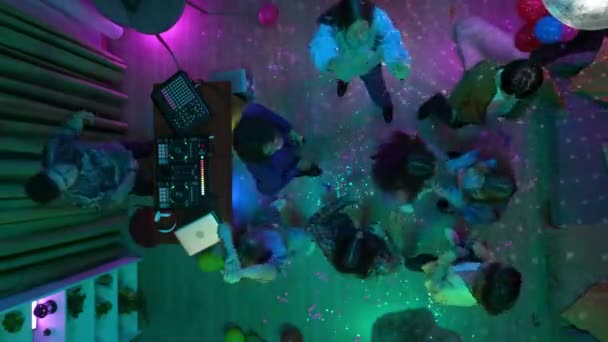 デコレーションされたパーティールームで踊るティーンエイジャーのグループとセルフィーを取る 男はDjコンソールで音楽を混ぜている ネオンライト トップビュー 高校年 大学年 クリエイティブコンテンツ — ストック動画