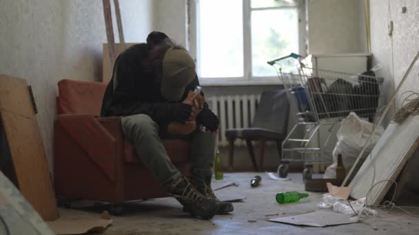 Άστεγος Άνθρωπος Κάθεται Ένα Δωμάτιο Ενός Εγκαταλελειμμένου Κτιρίου Γεμάτο Πενιχρά — Αρχείο Βίντεο