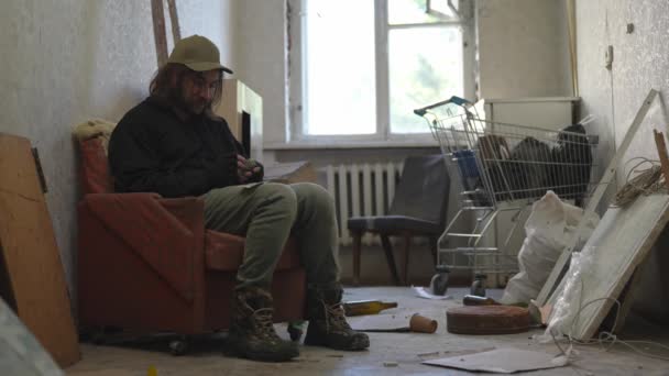 Bezdomny Biedak Siedzący Opuszczonym Budynku Wypełnionym Swoimi Skromnymi Rzeczami Liczy — Wideo stockowe