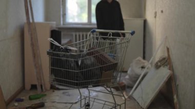 Evsiz bir adam işe yarar şeyler aramak için terk edilmiş bir binanın etrafında dolaşıyor. Eşyalarının alışveriş arabası ön planda duruyormuş. Evsizlik ve yoksulluk, işsizlik, kriz.