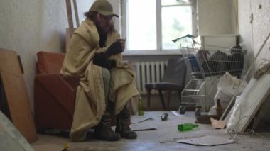 Terk edilmiş bir binanın odasında oturan evsiz zavallı adam. Battaniyenin altında ısınmaya çalışıyor, bir bardaktan sıcak içecek içiyor. Evsizlik ve yoksulluk, işsizlik, kriz.