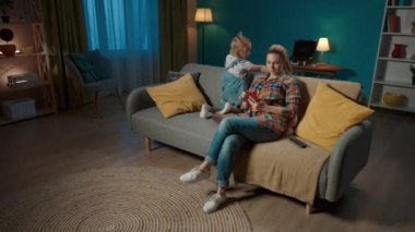 Genç bir kadın, bir anne, akıllı telefonuna dalmış ve kızına dikkat etmiyor. Anne ve kızı akşamları oturma odasında kanepede oturuyorlar. Ebeveynlik sorunları. SorunlarName