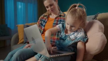 Annem kızına dizüstü bilgisayarda çalışmayı öğretiyor. Cihazın çalışma prensibini anlatıyor ve ona gösteriyor. Anne ve kızı oturma odasındaki kanepede oturmuş internette oyun oynuyorlar.