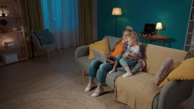 Mutlu, genç bir anne ya da dadı, genç kızıyla koltukta oturup dizüstü bilgisayarda video ve çizgi film izliyor. Anne ve kızı akşamları birlikte oturma odasında vakit geçiriyorlar.