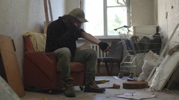 Άστεγος Άνθρωπος Κάθεται Ένα Δωμάτιο Ενός Εγκαταλελειμμένου Κτιρίου Γεμάτο Πενιχρά — Αρχείο Βίντεο