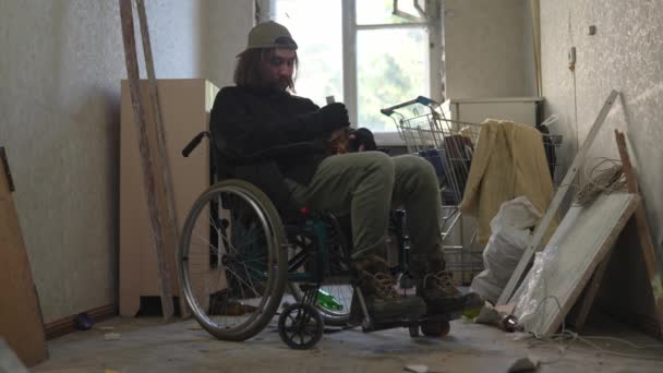 노숙자 가난한 남자는 자신의 빈약한 소지품으로 버려진 건물의 휠체어에 마시고 — 비디오