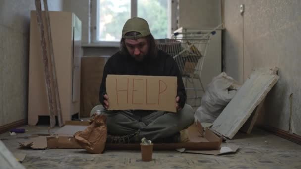 노숙자 가난한 남자는 항아리와 버려진 건물의 골판지 기호와 도움을 구걸하고있다 — 비디오