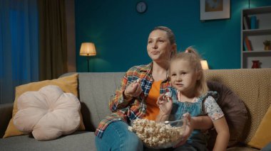 Mutlu anne oturma odasındaki kanepede oturmuş küçük kızıyla sarılıp televizyon izliyor ve büyük bir tabaktan patlamış mısır yiyor. Anne ve kızı gülüyor, komik bir film izliyor, çizgi film izliyor ya da