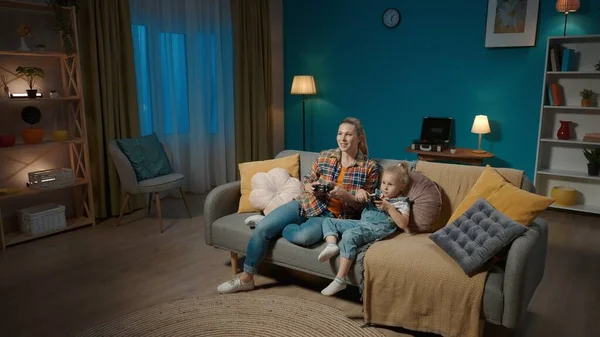 妈妈和小女儿用操纵杆玩电子游戏 妈妈和女儿整晚都坐在电视机前沙发上的客厅里 家庭父亲节概念 — 图库照片