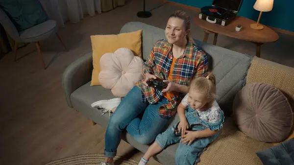 妈妈和小女儿用操纵杆玩电子游戏的头像特写 妈妈和女儿整晚都坐在电视机前沙发上的客厅里 家庭父母 — 图库照片