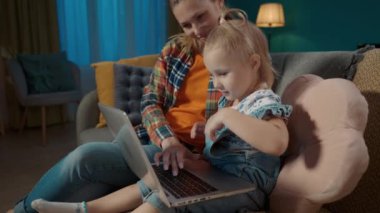 Bir anne küçük kızına bilgisayar uygulamalarıyla nasıl çalışacağını öğretiyor. Anne ve kızı oturma odasında kanepede oturup online oyun oynuyorlar, çocuklar için eğitim uygulamaları öğreniyorlar, daktilo yazıyorlar.