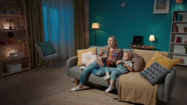 妈妈和小女儿用操纵杆玩电子游戏 妈妈和女儿整晚都坐在电视机前沙发上的客厅里 家庭父亲节概念 — 图库视频影像